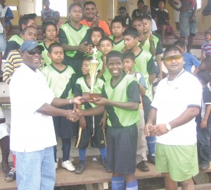 Captain of the winning team Mervyn Haywood receives the trophy from Ministry of Sport Parliamentary Secretary Steve Ninvalle (left), in the presence of Region Eight Regional Executive Officer, Ishwar Dass (right) and team members. 