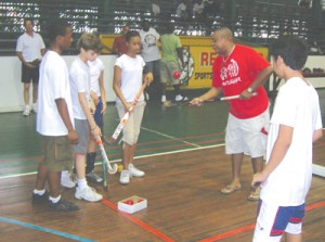 THIS IS HOW IT”S DONE!!! Hockey Coach,  Rawle Davson (centre) demonstrates one  of the skills drill to enthusiastic young players  yesterday at the Cliff Anderson Sports Hall.