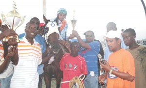 Champions all in a row!!! Champion horse Finishing Touch with Champion Jockey Kumar Singh on mount, while champion owner and trainer Mahendra Persaud (with phone) all savour the moment, as Ramesh Sunich (centre) of the Trophy Stall, Bourda Market presents the trophies.