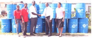  CEO of SOL Inc. Ken Figaro presents 30 drums to Milton Smith, President of the Young Leaders of Agricola, in the presence of group members and SOL’s Ayanna Wickham (extreme right).