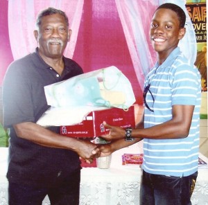 Basil Butcher (left) hands over the packages to Shimron Hetmyer of Young Warriors Cricket Club. 