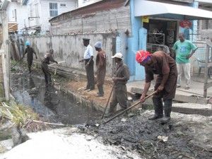 Prisoners desilting a drain under the watchful eye of a Prison Officer