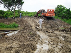 The excavator that was retrieved from the canal and the contractor walking on a board where there was a bridge.