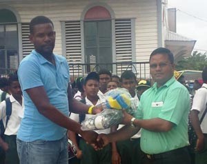 Godwyn Allicock handing over volleyballs and net to Rohan Etwaroo in the presence of students.