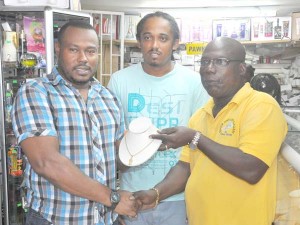 Proprietor of Junior’s Jewellery & Pawn Shop Ferdinand Bacchus (right) hands over the gift to Petra’s Troy Mendonca in the presence of Desibo Kumar yesterday.