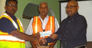 The cheque being handed over to Komal Singh by Suresh Narine. At centre is Walter Willis