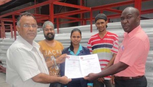 GNBS’s Mr Al Fraser (extreme right) hands over the renewal certificate to PPL’s Mr Bharrath Rampersad in the presence of support staff.