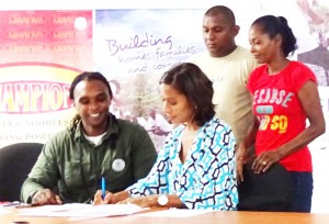 Anjelie Beharry-Strand signing the partnership agreement with Habitat’s National Director, Raul Small. Also in photo are beneficiaries Imran Khan and Sherry Bacchus.