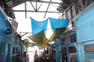 Vendors improvising at the collapsed section of the Stabroek Market Wharf yesterday during a brief downpour. 
