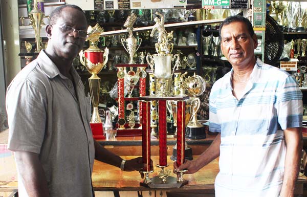 Chairman of the Boyce/Jefford Committee, Colin Boyce (left) receives some of the trophies that will be up for grabs Sunday from Proprietor of the Trophy Stall, Ramesh Sunich yesterday. 