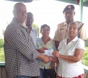 Mr. George Baijnauth hands over a cheque to Dolaria Goberdhan, whose house was razed by fire 