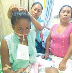  Onika Luke sitting on her bed with her aunt fixing her hair, while her mother stands to the right  