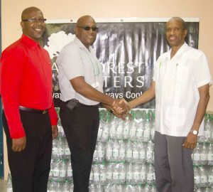 Dr. Douglas Slater Assistant Secretary General of Human and Social Development of Caricom Secretariat receives the donation from Rain Forest Water Brand Manager Clive Pellew, while Sherwin-Toyne-Stephenson of the CAIRCOM Secretariat looks on.