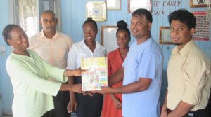 RHTY&SC Executive Mark Papannah hands over a copy of the Magazine to Deputy Head Teacher of Lower Corentyne Secondary School, Sharon Hawke in presence of other staff members. 