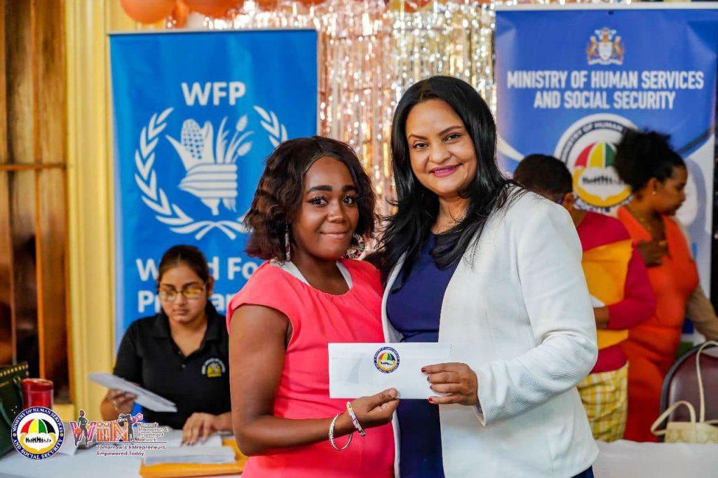 A woman receives a WIIN cheque from Minister of Human Services and Social Security Dr. Vindhya Persaud to assist in her start-up venture.