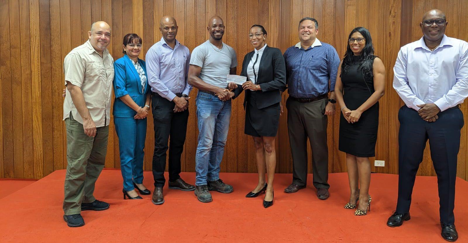 Vice-President Cristy Campbell (centre) hands over sponsorship cheque to Dwayne Scott who is flanked by Executive Members of the Guyana Olympic Association.  (From left) Mr. Michael Singh, Ms. Emily Ramdhani, Mr. Godfrey Munroe, Mr. Dwayne Scott, Mr. Philip Fernandes, Ms. Vidushi Persaud-McKinnon and Mr. Steve Ninvalle.