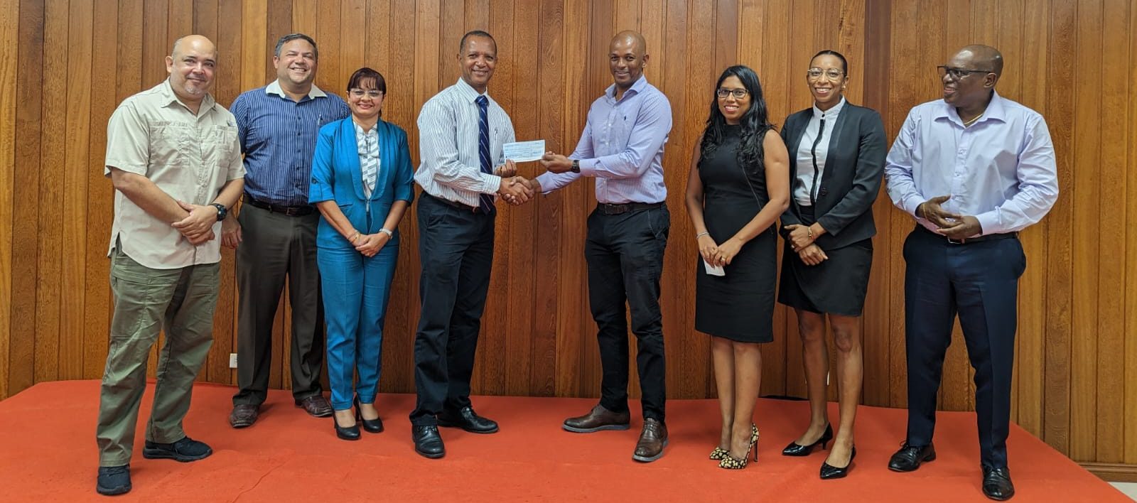 President Godfrey Munroe (centre) hands over sponsorship cheque to Aubrey Hutson, in the presence of Executive Members of the Guyana Olympic Association; from left - Michael Singh, Philip Fernandes, Emily Ramdhani, Hutson, Munroe, Vidushi Persaud-McKinnon, Cristy Campbell and Steve Ninvalle.