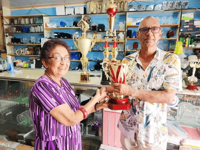 Mrs. Chan Kennard collects one of the trophies from Ramesh Sunich of the Trophy Stall.